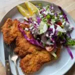 Chicken schnitzel l served on a place with a side salad.