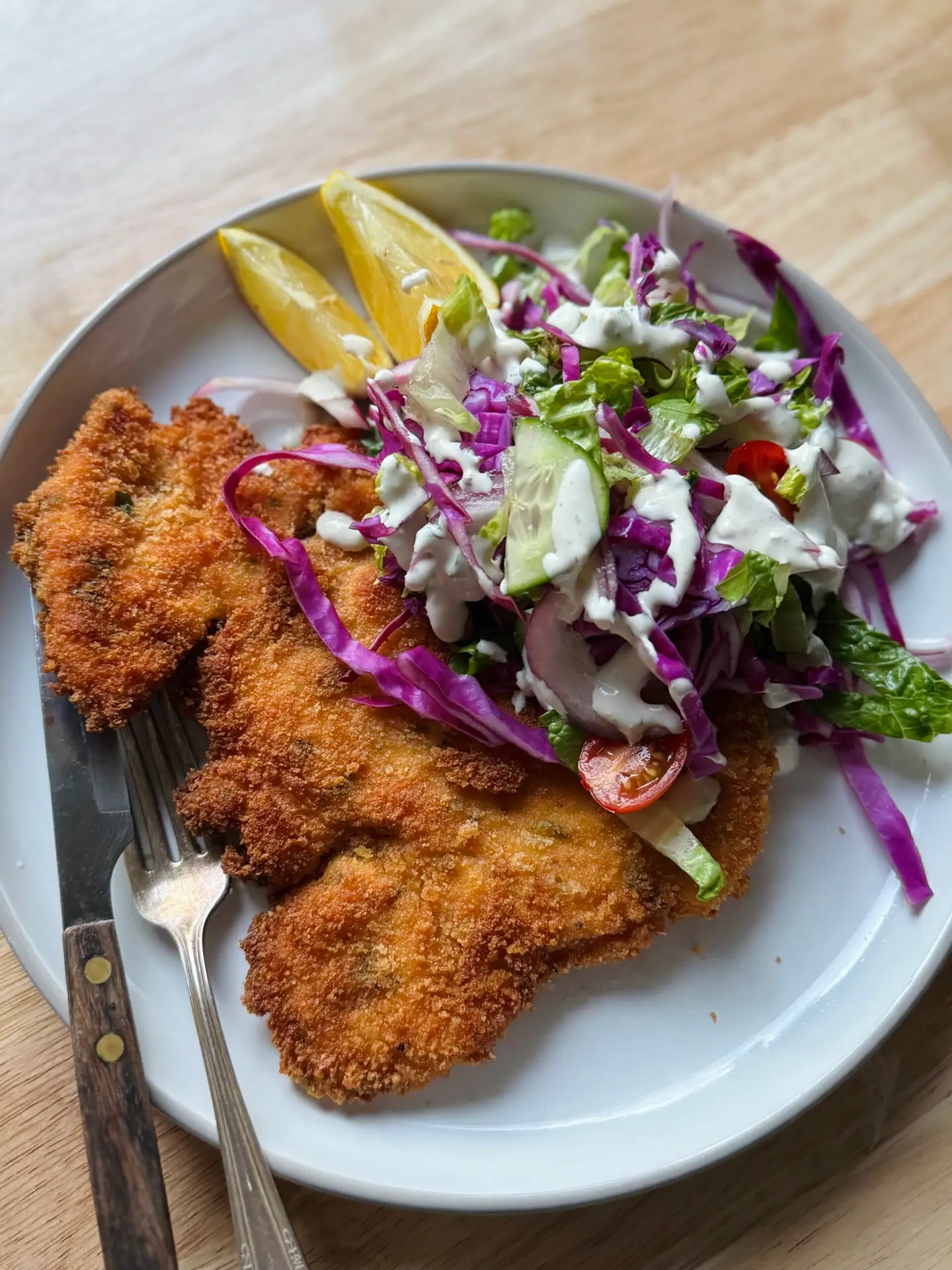 Chicken schnitzel l served on a place with a side salad.
