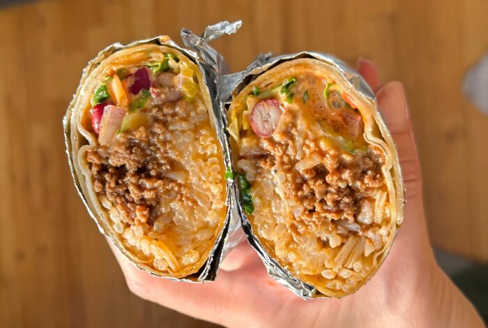 Cheesy beef burrito on white plate with shredded cabbage and chipotle sauce.