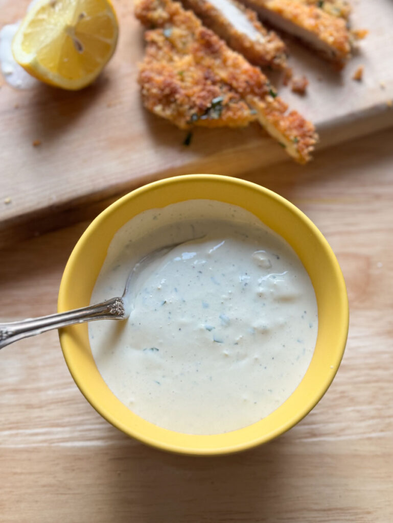 Chunky homemade blue cheese dressing in a yellow bowl with a spoon.