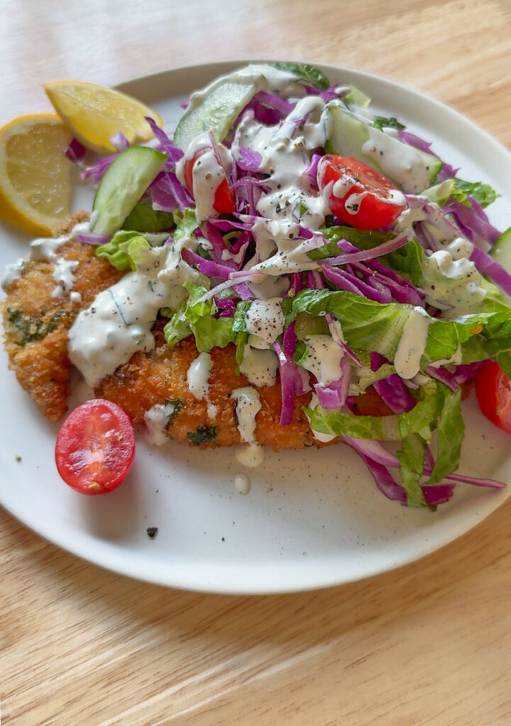 Crispy chicken schnitzel topped with homemade blue cheese dressing, served with fresh salad and lemon wedges.