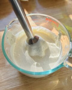 immersion blender mixing creamy blue cheese dressing in Pyrex measuring cup on wooden surface