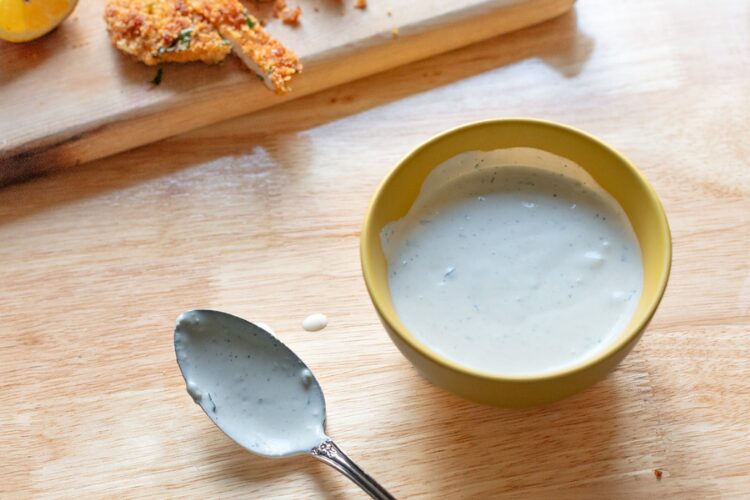 creamy blue cheese dressing in yellow bowl with spoon and crispy chicken on cutting board
