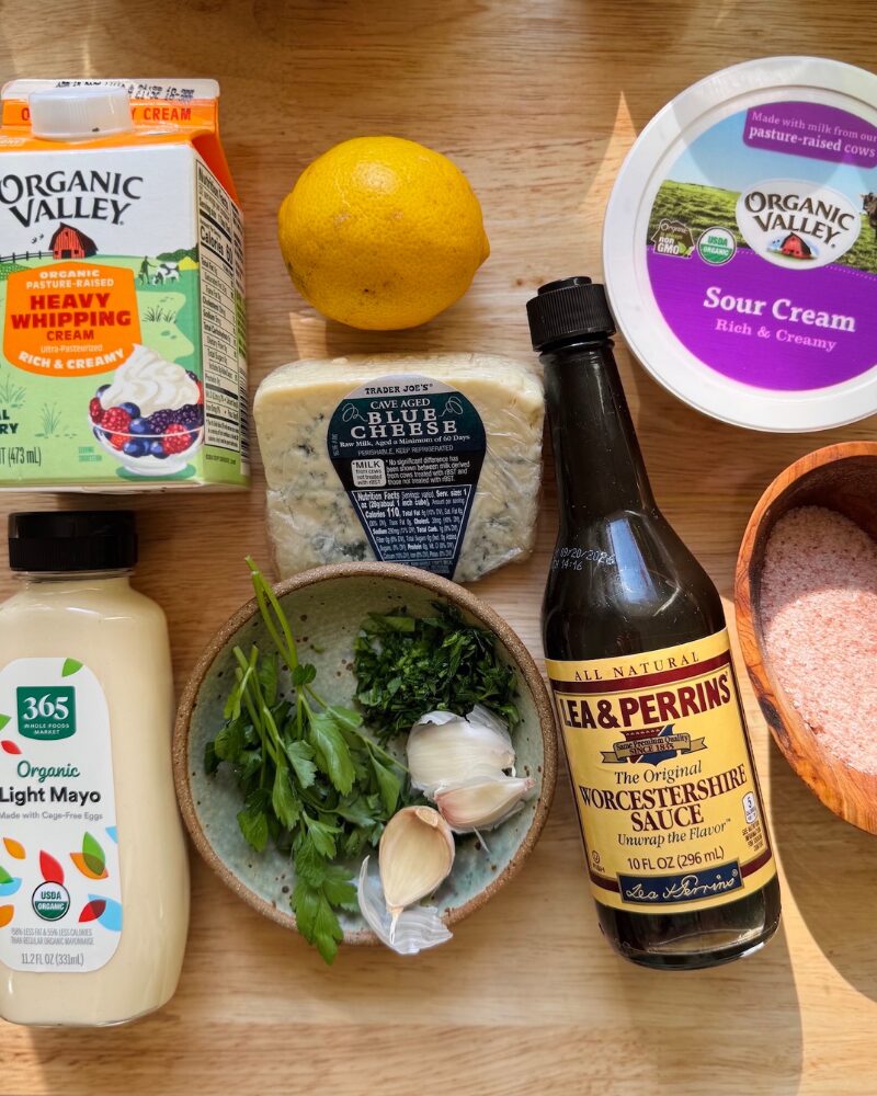 flat lay of blue cheese dressing ingredients including blue cheese, garlic, parsley, mayo, sour cream, lemon, and worcestershire sauce