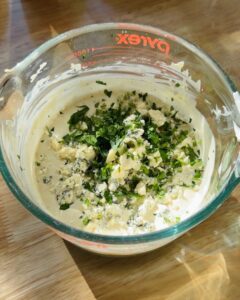 creamy blue cheese dressing with fresh herbs and crumbled cheese in a Pyrex measuring cup