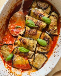 baked eggplant rollatini in tomato sauce, topped with fresh basil leaves and a serving spoon resting in the saucy dish
