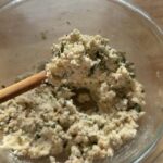 fully mixed herbed ricotta cheese filling in a glass bowl, scooped up with a wooden spoon, ready to stuff roasted eggplant slices