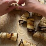 hands gently rolling roasted eggplant slices around a creamy ricotta filling on parchment paper
