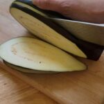 slicing eggplant lengthwise on a wooden cutting board