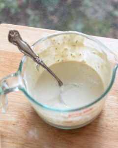 homemade blue cheese dressing in Pyrex measuring cup with spoon on wooden surface
