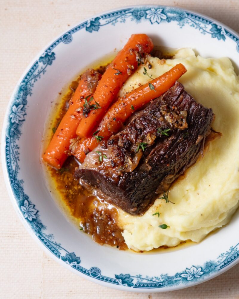 tender braised beef served with roasted carrots and creamy mashed potatoes, finished with a rich savory pan sauce on a blue-rimmed plate