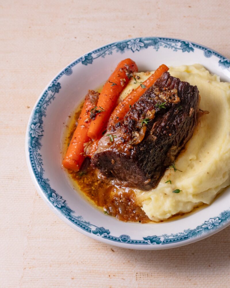 braised chuck roast served with tender carrots and creamy mashed potatoes, finished with a rich pan sauce on a blue-rimmed plate