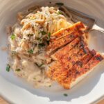 creamy parmesan pasta twirled in a rich, silky cheese sauce with freshly cracked black pepper and herbs, served in a white bowl alongside sliced seared chicken breast