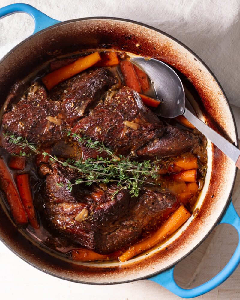 slow-braised chuck roast simmering in a dutch oven with carrots, fresh thyme, and rich savory braising liquid, ready to serve