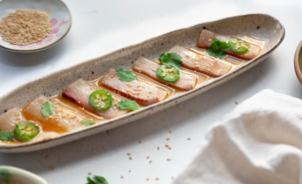 Hamachi crudo with ponzu, citrus, jalape&ntilde;o, and sesame seeds on a ceramic platter