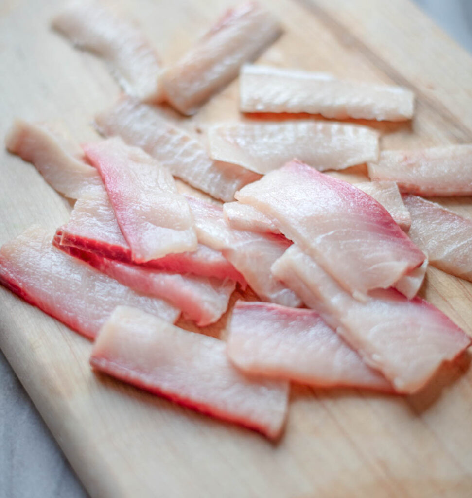 Sliced sashimi-grade yellowtail for hamachi crudo on a wooden cutting board