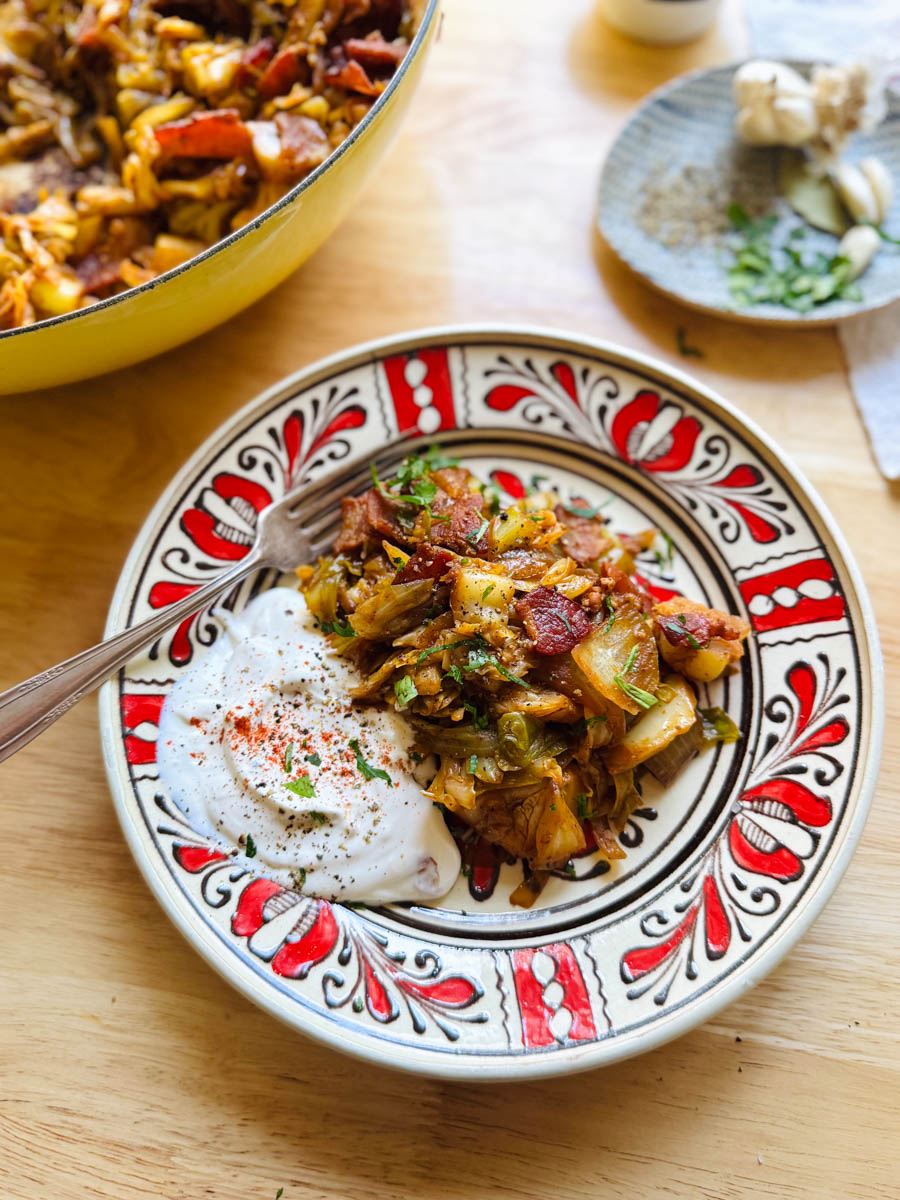 sauteed cabbage with crispy bacon and caramelized onions served with sour cream on a patterned plate