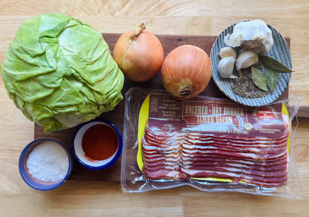 ingredients for sauteed cabbage with bacon including green cabbage, onions, garlic, bay leaves, paprika, and sliced bacon