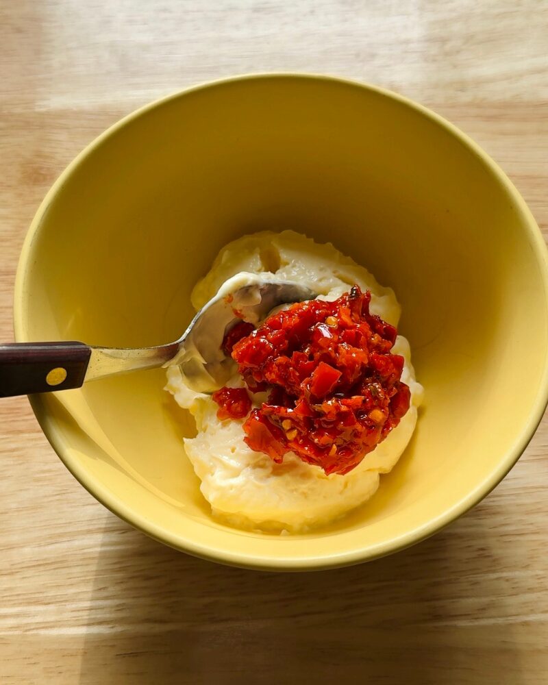 calabrian chili peppers being added to mayonnaise in a bowl before mixing