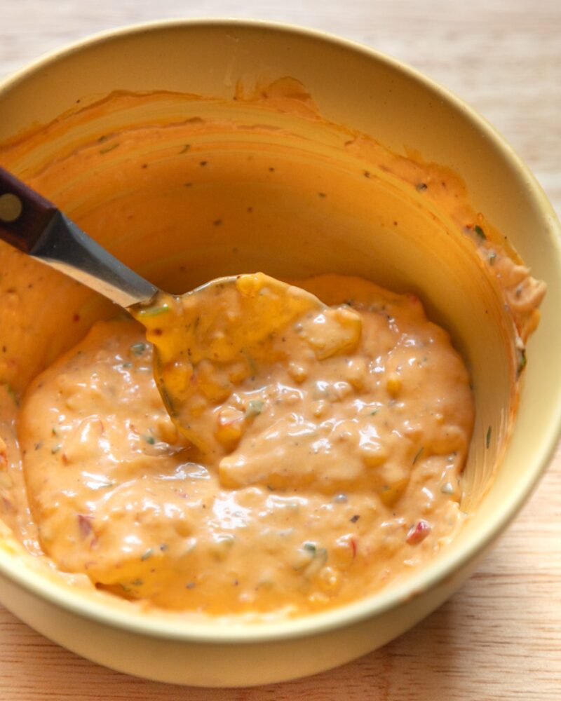 creamy calabrian chili mayo fully mixed in a yellow bowl with visible herbs and chili pieces