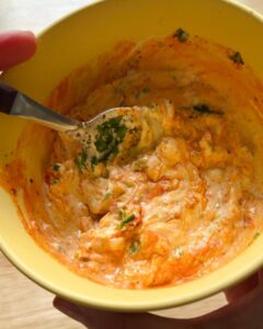 calabrian chili mayo being mixed in a yellow bowl with fresh herbs and visible chili oil swirled into the mayonnaise