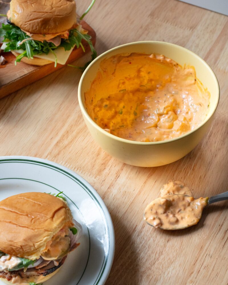 calabrian chili mayo in a small yellow bowl served alongside burgers with arugula and cheese
