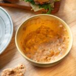 bowl of creamy calabrian chili mayo with visible chili pieces and herbs, served beside sandwiches