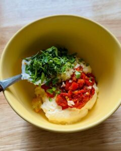 mayonnaise in a yellow bowl topped with calabrian chili peppers, minced garlic, and chopped fresh parsley before mixing