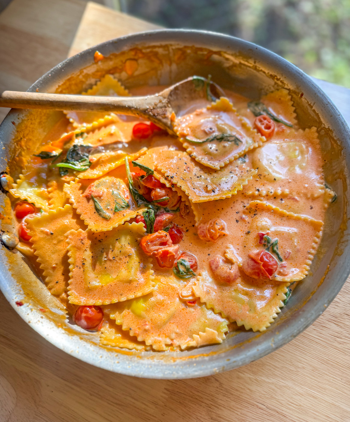 Creamy lobster ravioli sauce with sun-dried tomatoes and spinach in a skillet
