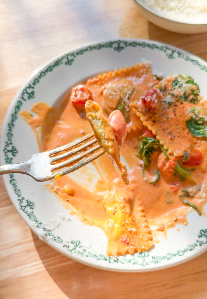 fork lifting lobster ravioli coated in creamy tomato sauce with spinach and cherry tomatoes