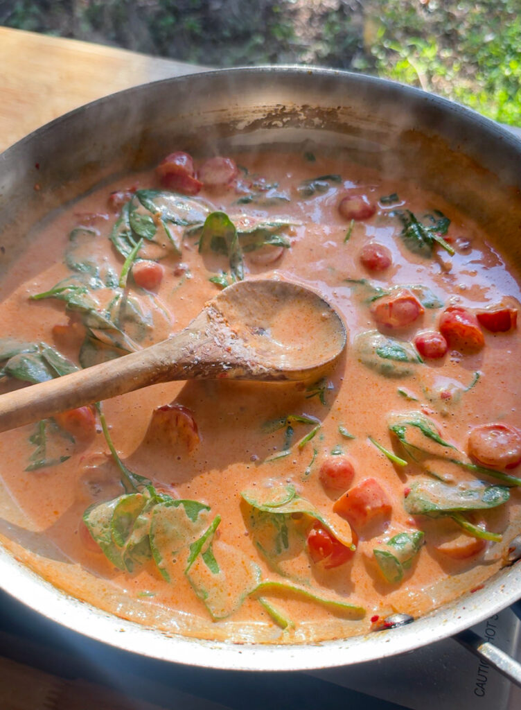 creamy lobster ravioli sauce with cherry tomatoes and spinach in skillet
