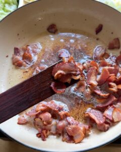crispy bacon cooking in a skillet, rendering fat for sauteed cabbage recipe