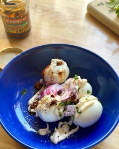 hard-boiled eggs topped with chili crisp, red onion, mayonnaise, and fresh herbs in blue bowl for spicy egg salad recipe