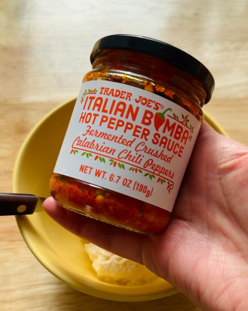 trader joe&rsquo;s italian bomba hot pepper sauce jar, fermented crushed calabrian chili peppers, held above a bowl of mayonnaise