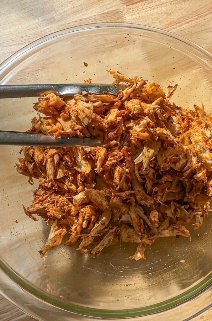 shredded chicken mixed with taco seasoning in a bowl for baked chicken tacos