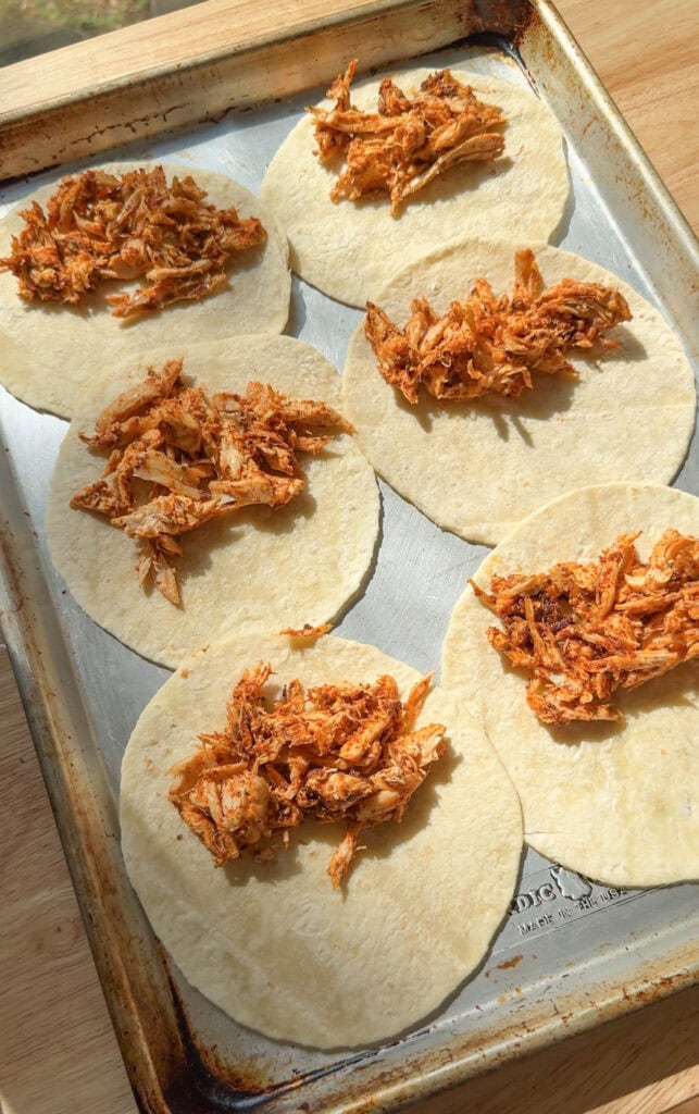 Shredded chicken added to tortillas on a sheet pan for baked chicken tacos