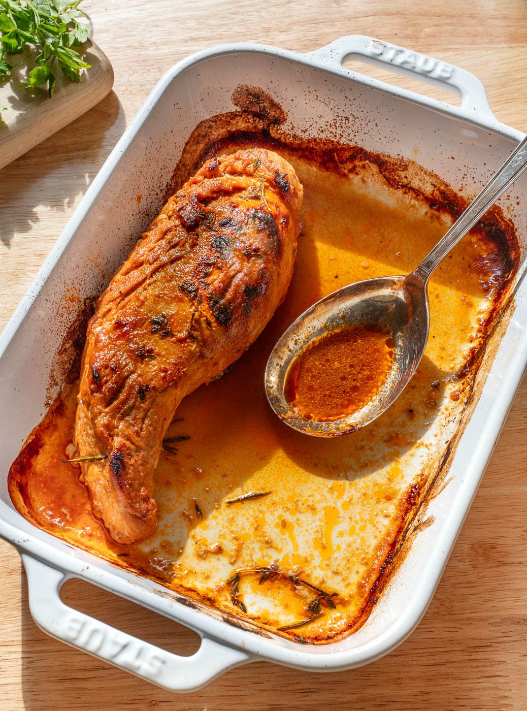 Pork tenderloin in a white baking dish with a spoon.