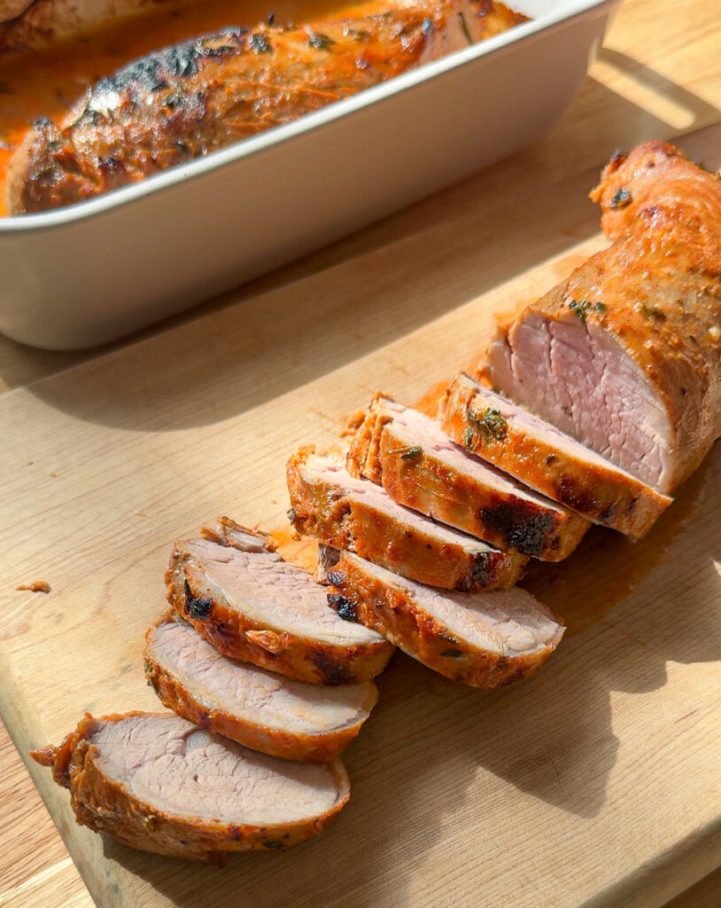 Sliced pork tenderloin on a wooden board.