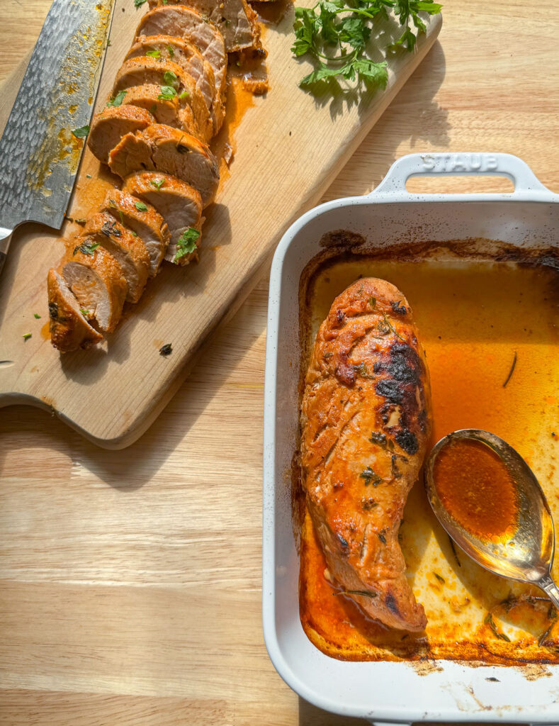 Baked pork tenderloin in a baking dish and one on a wooden board cut into slices.