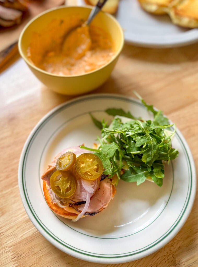 open-faced pork tenderloin slider with Calabrian chili mayo, arugula, pickled jalape&ntilde;os, and shallots on a toasted bun