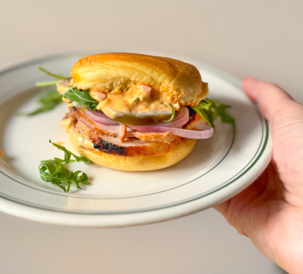 pork tenderloin slider with Calabrian chili mayo, arugula, pickled jalape&ntilde;os, and shallots on a toasted bun on a plate