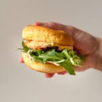 pork tenderloin slider with Calabrian chili mayo, arugula, and shallots on a toasted bun, held in hand