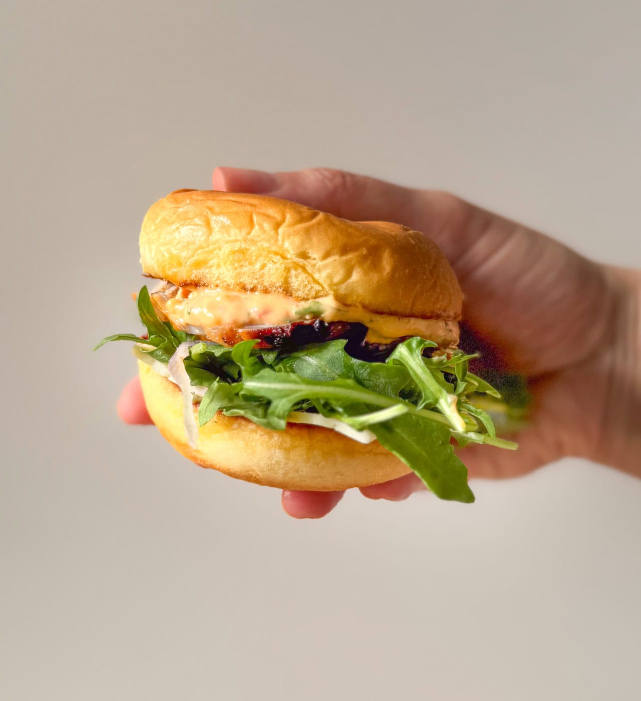 pork tenderloin slider with Calabrian chili mayo, arugula, and shallots on a toasted bun, held in hand