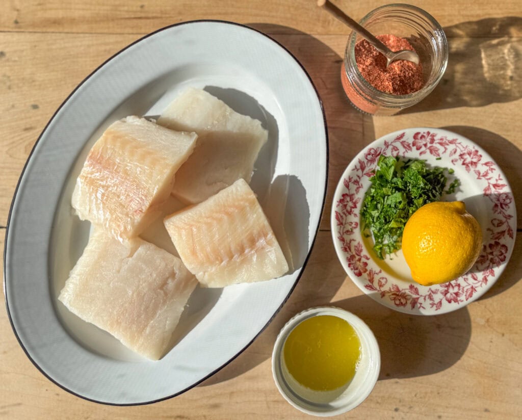 raw cod fillets with lemon parsley butter and paprika seasoning on wooden surface