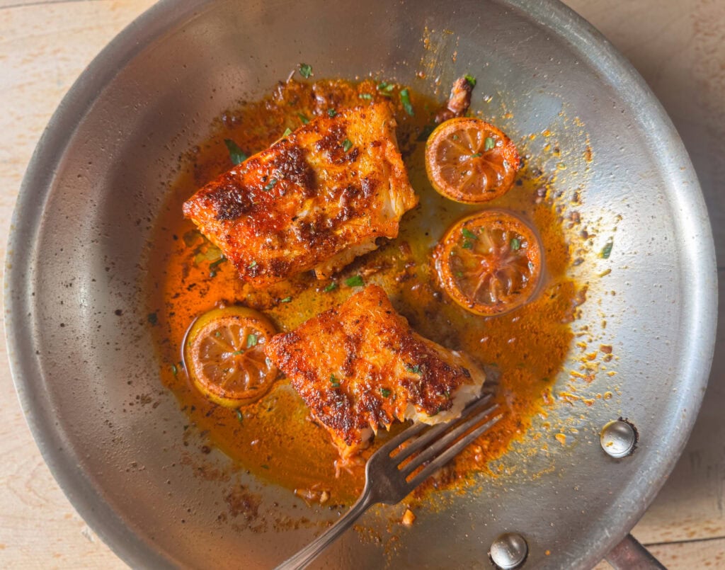 blackened cod in skillet with lemon slices and butter sauce