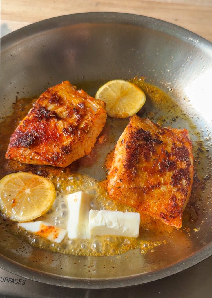 blackened cod fillets in skillet with butter melting and lemon slices