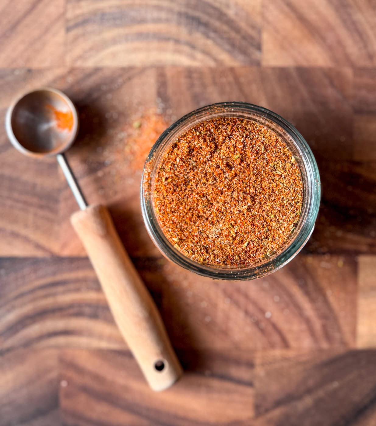 homemade chicken taco seasoning in a glass jar on a wooden board with measuring spoon