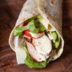 close up grilled chicken wrap with honey mustard sauce, avocado, tomato and lettuce