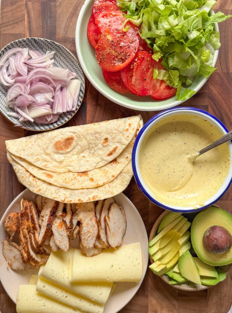 grilled chicken wrap ingredients with tortillas, sliced chicken, cheese, lettuce and tomato
