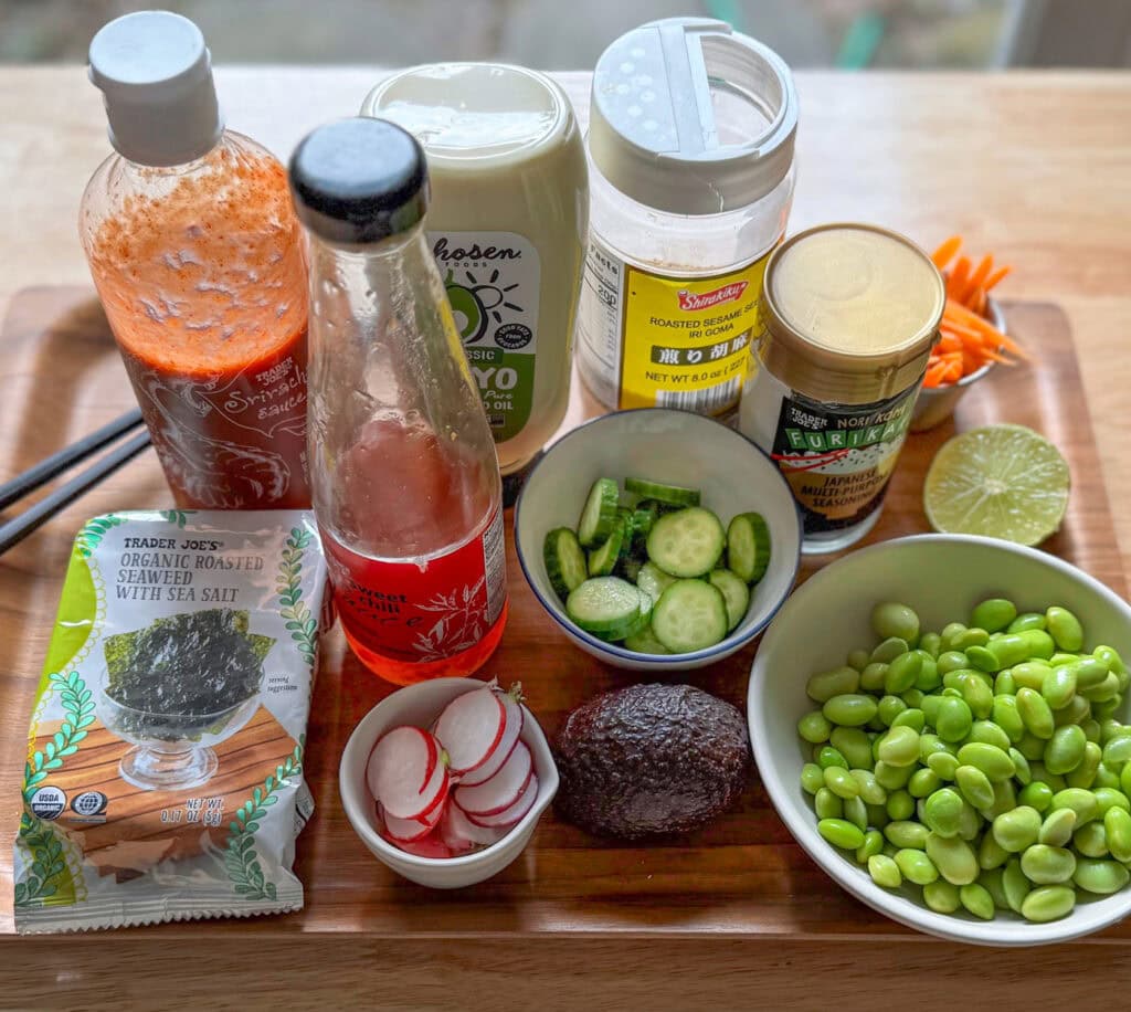 salmon rice bowl ingredients with spicy mayo, avocado, cucumber, and edamame